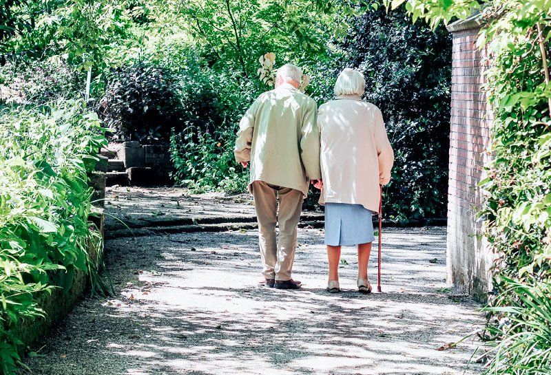 Pareja de personas mayores con bastón paseando por jardín en Residencia Las Cumbres